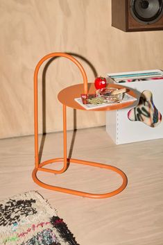 an orange table sitting on top of a wooden floor next to a speaker and rug