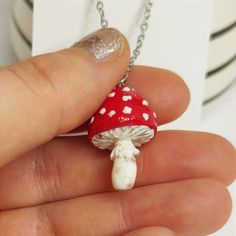 a tiny red and white mushroom necklace on a silver plated chain with a hand holding it