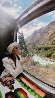 a woman looking out the window of a train with mountains in the backgroud