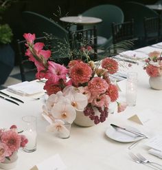 the table is set with pink and white flowers in vases on top of it