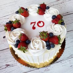 a white cake with strawberries and blueberries on top sits on a wooden table