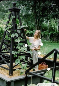 a woman standing next to a tall wooden structure with plants growing on it's sides