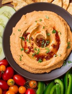 a black plate topped with hummus next to vegetables and crackers