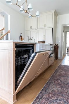 an open dishwasher sitting on top of a wooden floor next to a rug