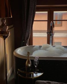 a bath tub filled with bubbles next to a wine bottle and two glasses on a table