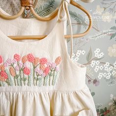 a white dress with pink flowers is hanging on a hanger next to a floral wallpaper