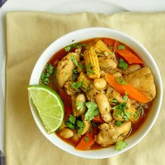 a white bowl filled with chicken and vegetables next to a slice of lime on top of a napkin