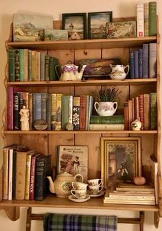 an old wooden shelf with books and tea cups on it, next to a plaid blanket