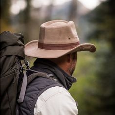 a man with a backpack and hat walking in the woods looking at something behind him