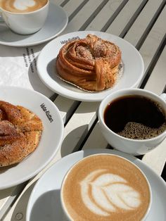 there are three plates with pastries on them and two cups of coffee next to each other