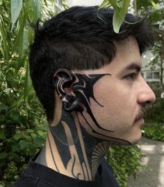 a man with tattoos on his face and neck is standing in front of some bushes