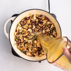 someone pouring olives into a skillet filled with food