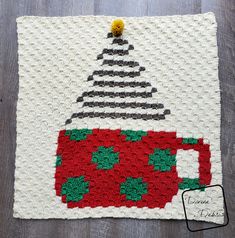 someone is holding up a crocheted coffee mug mat with a christmas tree on it