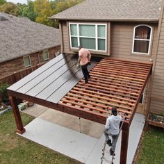 two men working on the roof of a house that is being built with wooden slats