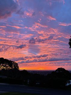 the sky is pink and purple as the sun sets in the distance behind some trees