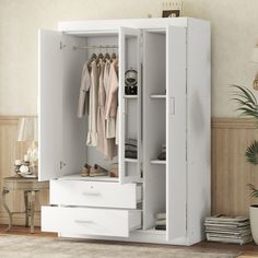 a white wardrobe with drawers and clothes hanging on the wall next to a potted plant