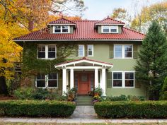 a green house with red roof and white trim on the front door is surrounded by trees