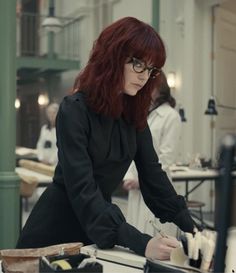 a woman with red hair and glasses working on something