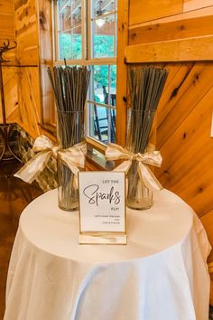 two vases with sticks in them on top of a white table cloth covered table