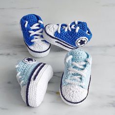 three crocheted blue and white sneakers are on a marble surface, one is for toddlers