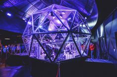 people are standing in front of a large glass structure with blue lights on the ceiling