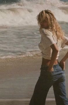 a woman walking on the beach next to the ocean