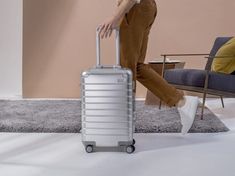 a woman in brown pants and white sneakers pulling a silver suitcase with wheels on the floor