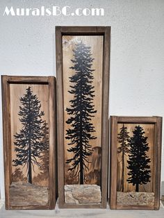 three wooden frames with black and white pine trees on them, one has a rock in front of it