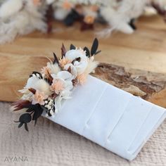 a white napkin with flowers on it sitting on top of a wooden table next to feathers