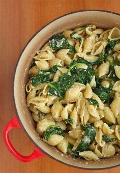 a pot filled with pasta and spinach on top of a wooden table