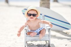 a small child sitting in a chair on the beach wearing sunglasses and a straw hat