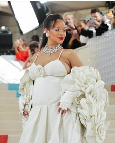 a woman in a white dress with flowers on her head walking down the stairs at a fashion show