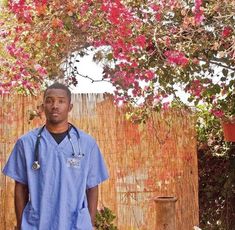 a man in scrubs standing under a tree with flowers on the wall behind him