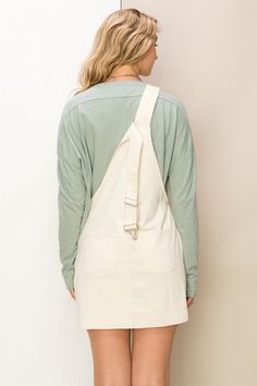 a woman with an apron on is looking down at her back while standing in front of a white wall