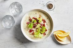 a bowl of soup with lettuce, bacon and lemon wedges on the side