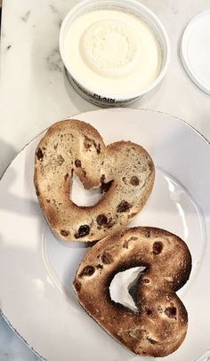 two chocolate chip heart shaped bagels on a plate next to a bowl of yogurt