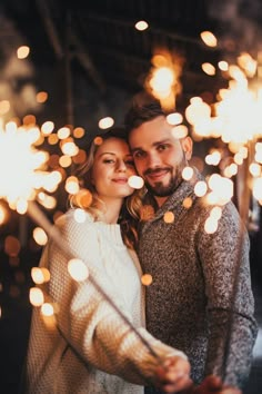 a man and woman standing next to each other with sparklers in the air behind them