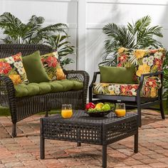 two wicker chairs and a coffee table with fruit on it in front of a house