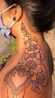 the back of a woman's neck with henna tattoos on it and flowers