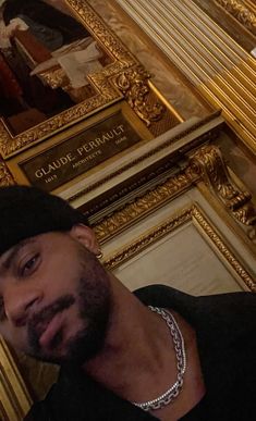 a man wearing a black hat standing in front of a gold framed portrait on the wall