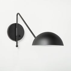 a black wall light mounted on the side of a white wall next to a lamp