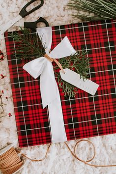 a red and black plaid wrapping paper wrapped in white ribbon, tied with twine