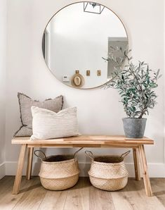 a wooden bench with two baskets underneath it and a round mirror on the wall