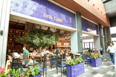 people are sitting at tables in front of a coffee shop with blue planters on the outside