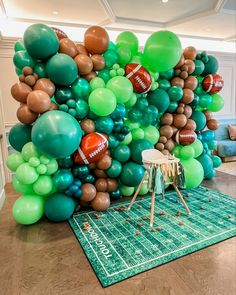 a football themed balloon wall in the middle of a room filled with green, brown and white balloons