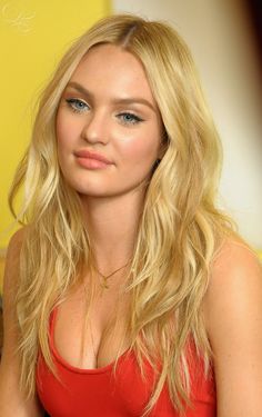 a woman with long blonde hair and blue eyes sitting on a couch looking at the camera