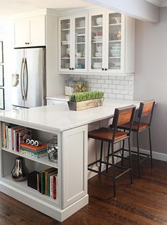 a kitchen with white cabinets and an island that has chairs on it, next to a refrigerator