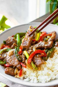 a white plate topped with meat and vegetables on top of rice next to chopsticks