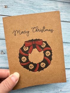 a hand holding up a christmas card with skulls and a wreath on it, which reads merry christmas