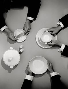 four people are holding plates and cups in the middle of a table with their hands on them